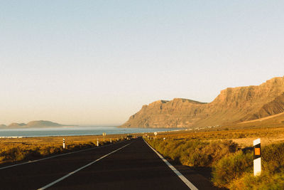 Empty road leading towards mountains against clear sky