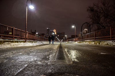 Friends walking on illuminated bridge against sky at dusk