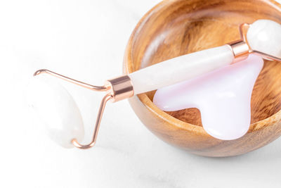 Pink guasha massage tool and scrapper in wooden bowl on marble background. rose quartz jade roller