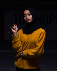 Portrait of woman in hijab standing against black background