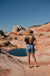 Rear view of man standing at desert against clear sky