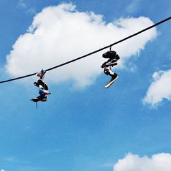 Low angle view of footwear hanging from cable against sky