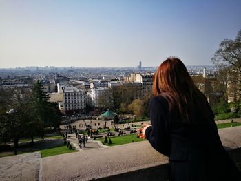 Rear view of woman standing on retaining wall against clear sky