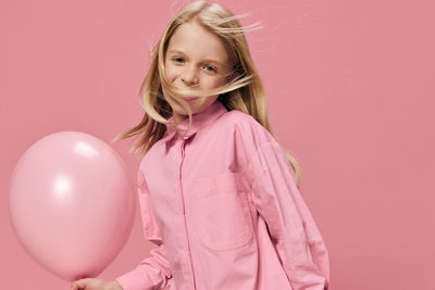 Portrait of young woman with balloons against pink background