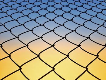 Full frame shot of chainlink fence against sky during sunset