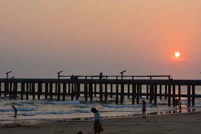 Silhouette people standing at beach against clear sky during sunset