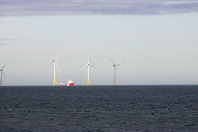 Wind turbines by sea against sky