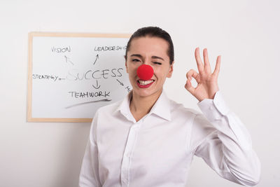 Portrait of businesswoman wearing clown nose while gesturing ok at office