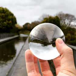 Close-up of hand holding crystal ball against glass