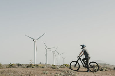 Side view of man riding bicycle on field against clear sky