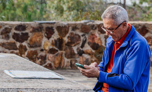 Senior man looking and touching screen of smartphone while sitting on park