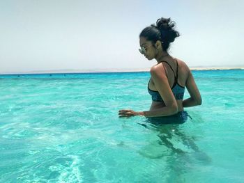 Rear view of young woman swimming in sea against clear sky