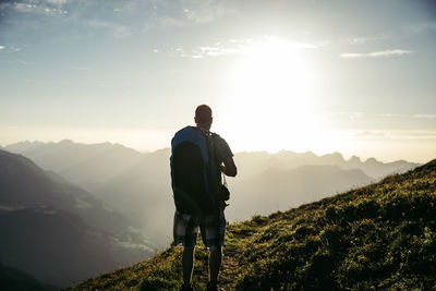 Rear view of male hiker looking at mountains against sky during sunset