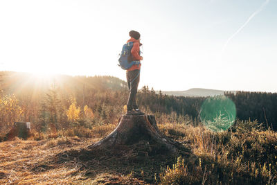 Active hiker standing on a stump enjoys the feeling of reaching the top of the mountain at sunrise