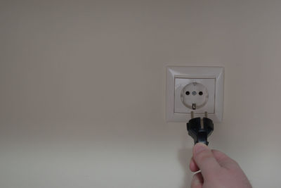 Close-up of hand holding electric light against wall