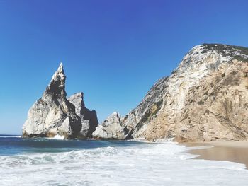 Rock formations in sea against clear blue sky