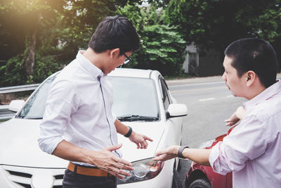 Young man holding camera while standing by car