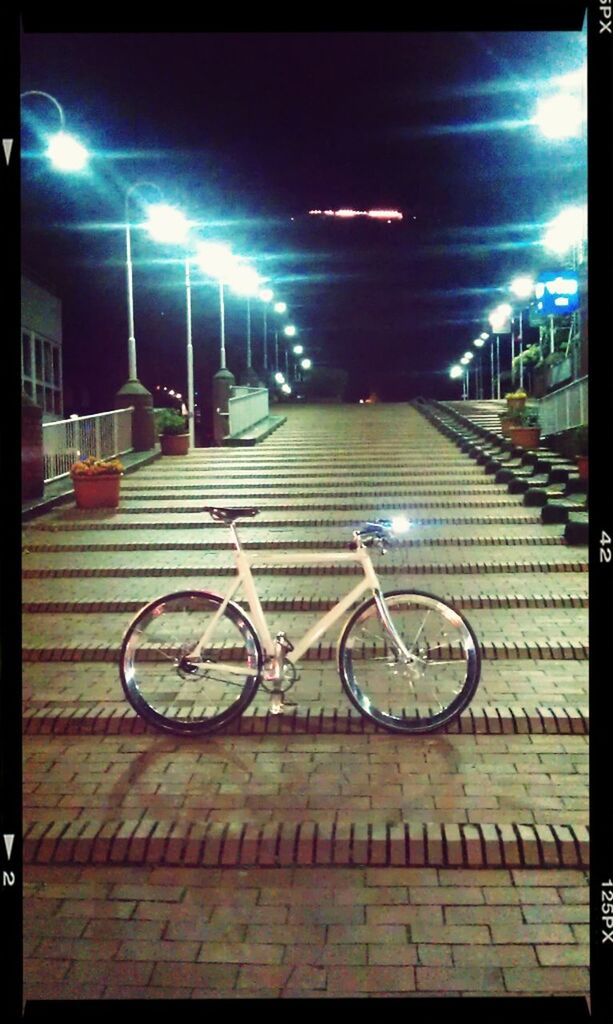 transportation, illuminated, night, mode of transport, transfer print, land vehicle, bicycle, street, street light, auto post production filter, building exterior, road, built structure, the way forward, architecture, sky, city, car, stationary, road marking