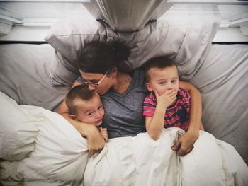 Directly above shot of boys with mother lying on bed