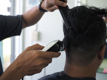 Cropped hands of barber cutting male customer hair in shop