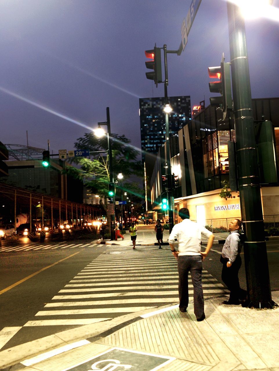 building exterior, illuminated, architecture, city, built structure, men, city life, street, walking, night, lifestyles, person, large group of people, street light, lighting equipment, transportation, zebra crossing, city street, leisure activity