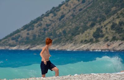 Shirtless boy running on shore at beach