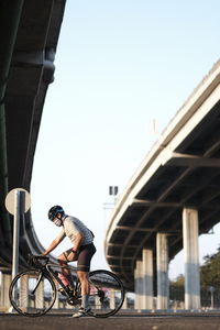 Man riding bicycle on bridge against clear sky