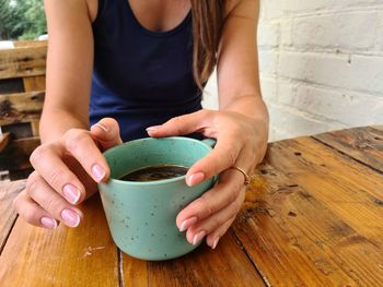 Midsection of woman holding coffee cup on table