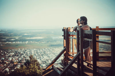 Man photographing on railing against sky