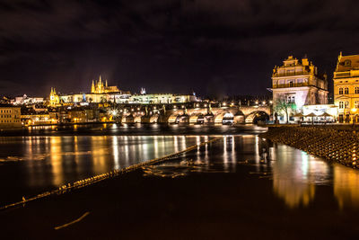 Illuminated buildings by river against sky in city at night