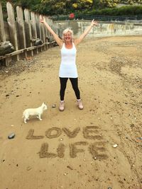 Smiling woman with arms raised standing by text at beach