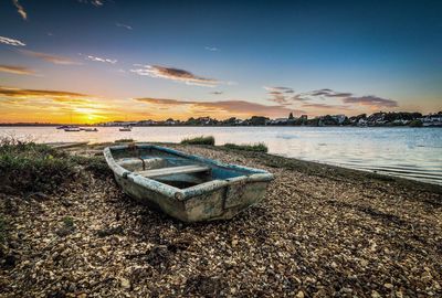 Abandoned boat moored on beach against sky during sunset