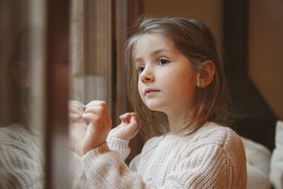 Close-up of cute girl looking through window at home