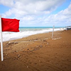 Red flag on beach against sky