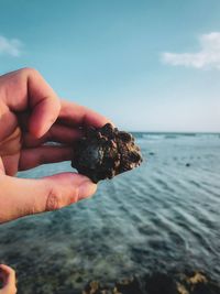 Close-up of hand holding rock over sea against sky
