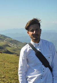 Front view of a indian young guy looking at camera while standing against in the nature 