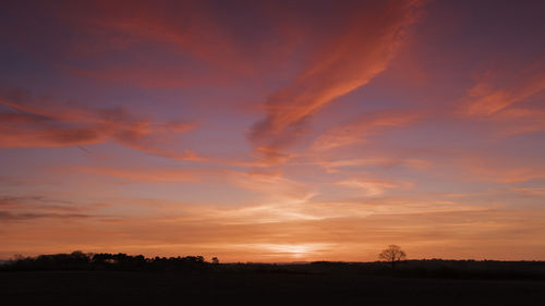 Scenic view of silhouette field against orange sky