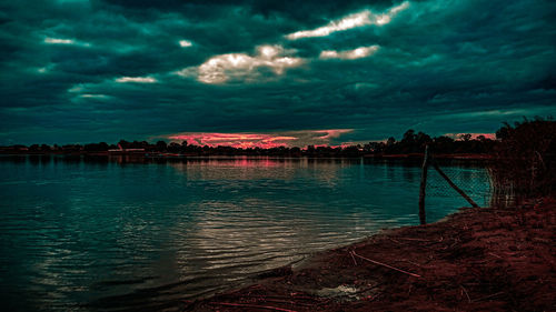 Scenic view of lake against dramatic sky during sunset