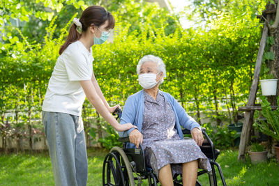 Caregiver help and care asian senior woman patient wearing mask sitting on wheelchair 