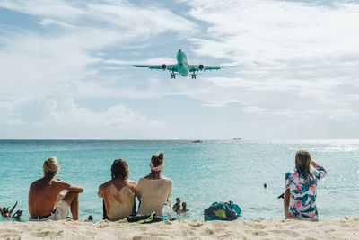 Rear view of women sitting at sea shore against sky