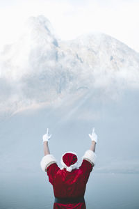 Rear view of man wearing santa claus costume looking at lake during foggy weather