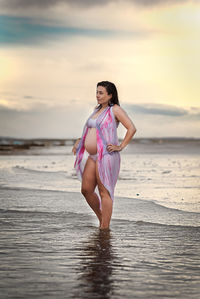 Full length of woman standing at beach against sky