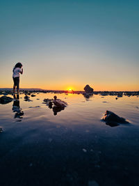 Rear view of woman walking on beach against sky during sunset