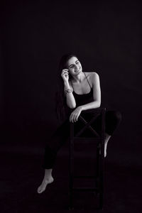 Young woman sitting on chair against black background