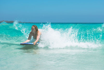 Young woman surfing in sea against clear blue sky
