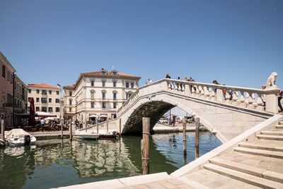 Arch bridge over river by buildings against clear sky