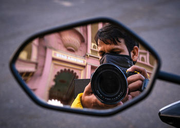 Reflection of man photographing on side-view mirror of car