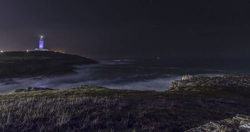 Illuminated lighthouse by sea against sky at night