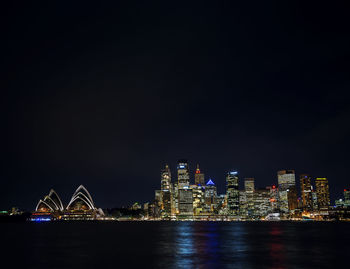 Illuminated city by river against sky at night