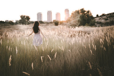 Rear view of young woman walking on grassy field during sunset